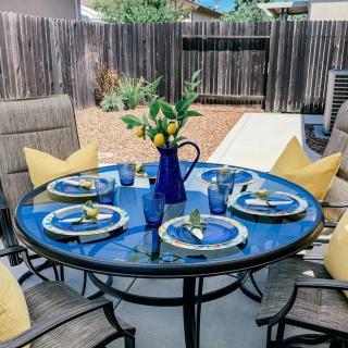 A stylish outdoor patio setup with a round glass table adorned with blue tableware, lemon-themed decoration, and cozy yellow pillows on the chairs.