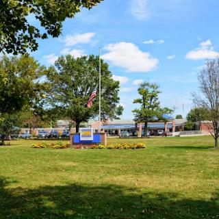A peaceful park setting featuring a flagpole, lush grass, and trees under a blue sky.