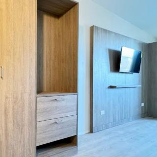 A modern, minimalist bedroom interior featuring a wooden wardrobe and a wall-mounted television.