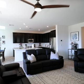 Modern open-concept living room and kitchen with black sofas and a ceiling fan.