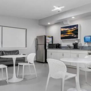 A modern break room with tables, chairs, a kitchenette, and a television.