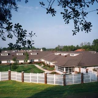A scenic view of a large house with a white fence, surrounded by greenery and trees.