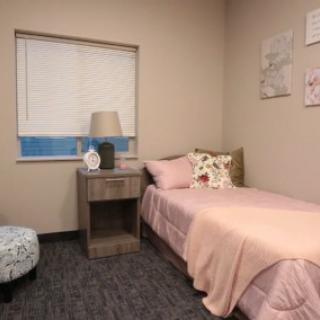 A cozy bedroom with a single bed and nightstand, featuring pastel decor.