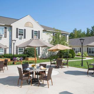 A sunny outdoor patio area with tables, chairs, and umbrellas in front of a building.