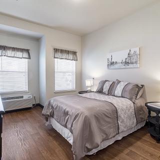 A modern, minimalist bedroom with a neatly made bed and wooden flooring.