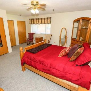 A cozy bedroom with a wooden bed frame featuring red bedding, surrounded by wooden furniture including a dresser and mirror.