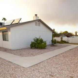 A suburban house with solar panels on the roof and a gravel yard.