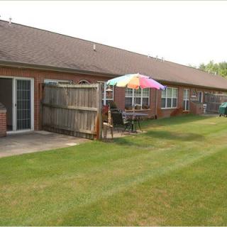 A row of brick houses with backyards featuring patios, outdoor furniture, and colorful umbrellas.