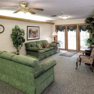 A cozy living room with green sofas, carpet flooring, and a ceiling fan.