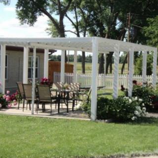 A backyard patio area with a white pergola and outdoor furniture surrounded by greenery.