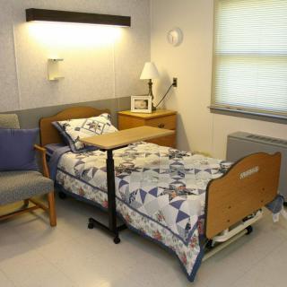 A hospital room featuring a single bed with bedding, a side table, and a lamp.