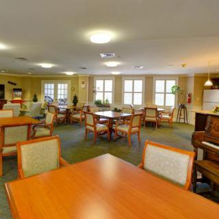 A spacious dining room with multiple tables and chairs, well-lit by large windows.