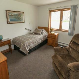 A cozy bedroom with a single bed and an armchair next to a window.