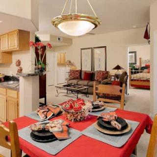 A cozy apartment interior featuring a dining table with vibrant red accents, an adjacent living room, and an open kitchen layout.