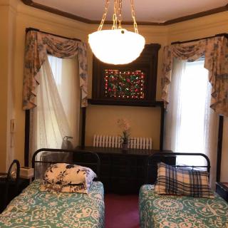 A vintage-styled bedroom with twin beds, ornate curtains, and a chandelier.