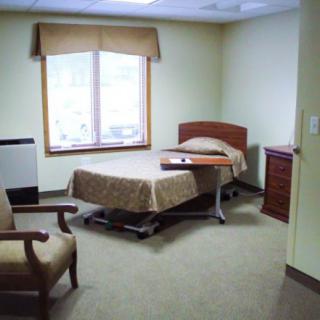 A simple and clean hospital or care facility room with a single bed, chair, and window.