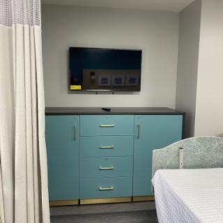 A view of a modern hospital room featuring a turquoise storage unit and a television mounted on the wall.