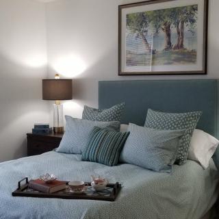 A cozy bedroom featuring a plush bed with multiple pillows, a bedside lamp, and artwork on the wall.