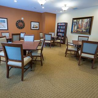 A well-lit conference room with multiple tables and chairs, adorned with artwork and a bookshelf.