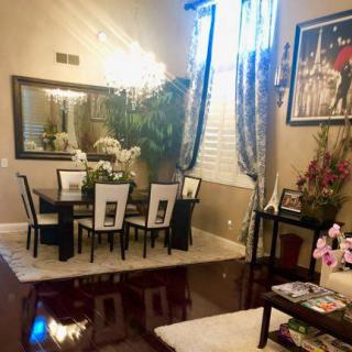 A beautifully decorated dining room featuring a large mirror, chandelier, and elegant furniture with decorative plants and artwork.