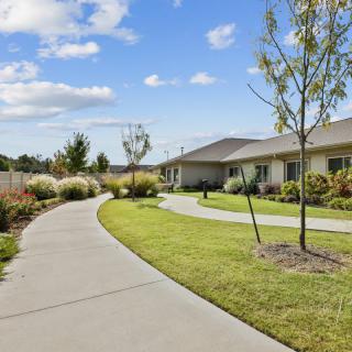 A scenic view of a building with a winding pathway, surrounded by well-maintained landscaping and trees under a blue sky with clouds.