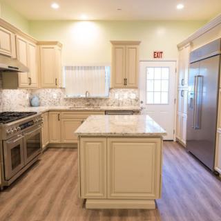 A modern kitchen with light wooden cabinets, an island counter, stainless steel appliances, and marble countertops.