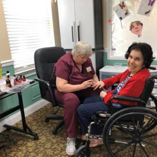 A caregiver providing a manicure to a resident in a wheelchair, showcasing the importance of personal care in senior living.