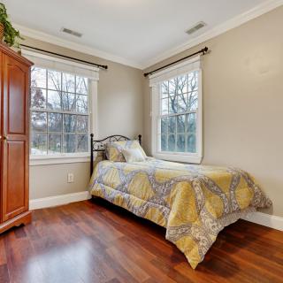 A cozy bedroom with a single bed, wooden floors, and large windows allowing natural light.
