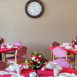 A dining room with tables set with red tablecloths and floral centerpieces, under a wall clock.