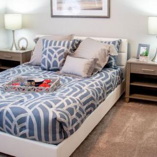A cozy bedroom with a neatly made bed featuring patterned bedding and pillows, flanked by wooden nightstands with lamps.