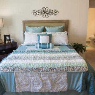 A neatly arranged bedroom featuring a bed with blue and white bedding, decorative pillows, and a bedside lamp.
