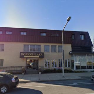 A street view of a building with a storefront and parked cars during the day.
