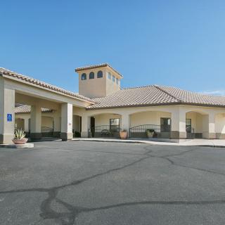 The exterior entrance of a hotel with an adjacent parking lot on a clear day.