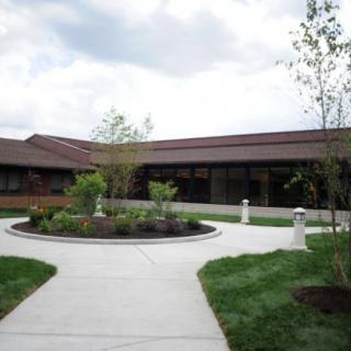 A landscaped garden with a central pathway leading to a modern building under a cloudy sky.
