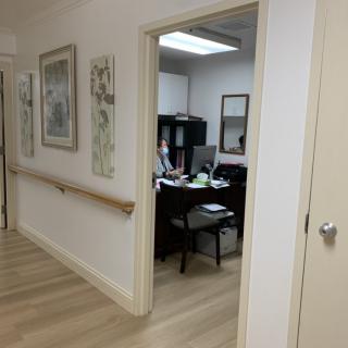 A view of an office through a hallway, featuring a desk with a computer and artwork on the walls.