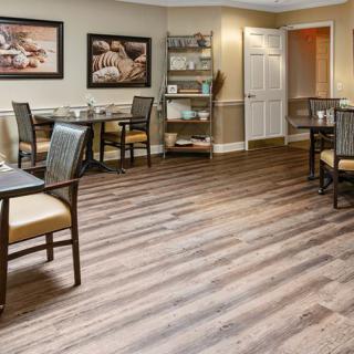 A beautifully arranged dining room with wood flooring, elegant chairs and tables, complemented by artistic wall decor and shelving.
