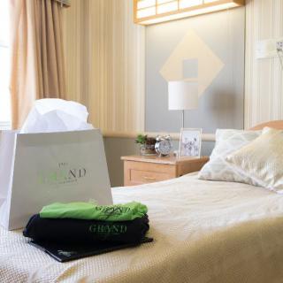 A cozy hotel room with a bed and a gift bag on it, softly lit by a nearby lamp.