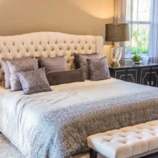 A cozy bedroom featuring a tufted headboard, decorative pillows, and a bedside lamp.