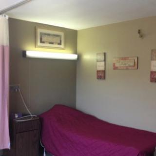 A simple bedroom featuring a single bed with a burgundy cover, wall-mounted lighting, and framed decor.