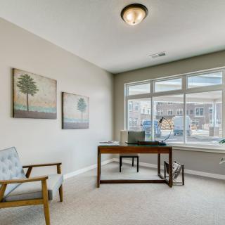 A modern office space with a wooden desk, armchair, and large window providing natural light.