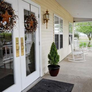 A welcoming front porch with decorative wreaths on double doors, a planter with greenery, and rocking chairs for outdoor relaxation.