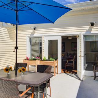 A sunny patio with a dining table, blue umbrella, and sunflowers by sliding doors.