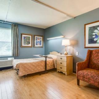 A well-furnished bedroom with a single bed, bedside table, lamp, and an armchair.