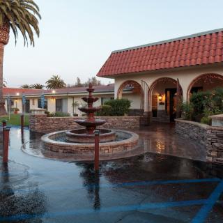 A peaceful hotel courtyard featuring a central fountain surrounded by arched walkways and tiled roofs.