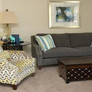 A cozy living room with a grey sofa, patterned armchair, wooden coffee table, and decorative elements.