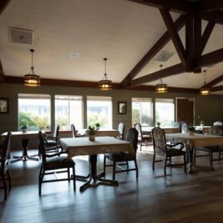 A cozy dining area with neatly arranged tables and chairs, featuring large windows and exposed wooden beams.
