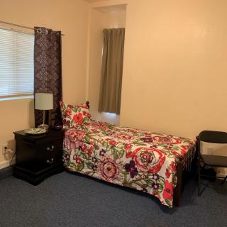 A cozy bedroom with a single bed adorned with colorful bedding, accompanied by a nightstand and lamp.