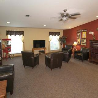 A cozy living room featuring several armchairs around a television, with a carpeted floor and warm lighting.