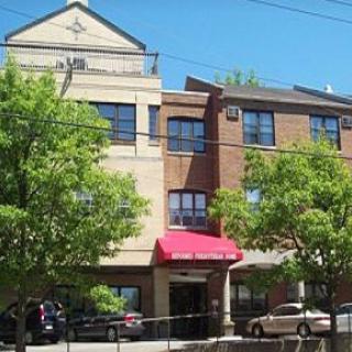 A three-story residential building with a red awning, surrounded by trees on a sunny day.