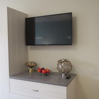 A wall-mounted television above a cabinet with decorative items including a bowl of apples and a decorative ornament.